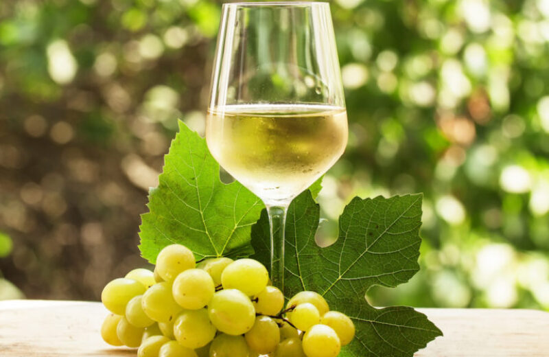 Coid white wine and green grapes on natural blurred background with bokeh, selective focus